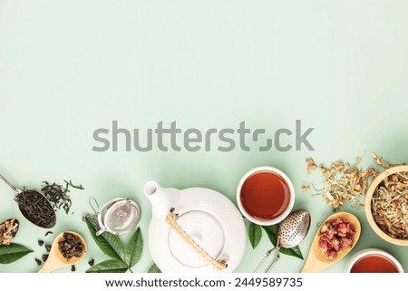 A well-arranged flat lay featuring a variety of loose-leaf teas, a white teapot, and tea accessories on a soft pastel green background, depicting a serene tea preparation scene.