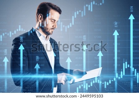 Attractive young businessman using tablet with growing blue vertical arrows and candlestick forex chart on blurry index grid background. Economic growth and increase concept. Double exposure