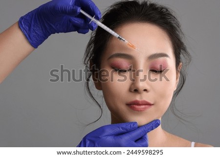 Woman getting facial injection on grey background