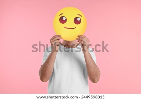 Man covering face with smiling emoticon on pink background