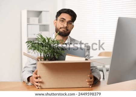 Unemployment problem. Frustrated man with box of personal belongings at desk in office Royalty-Free Stock Photo #2449598379