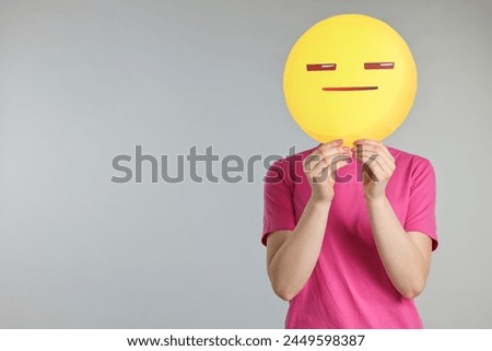 Woman holding emoticon with closed eyes and mouth on grey background. Space for text
