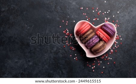 Various colorful macaroons in heart shaped bowl. Love sweets over stone background with copy space