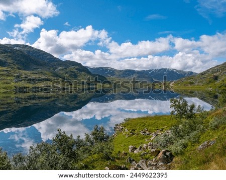 Reflection in the blue water of the mountains on the Gaularfjellet National Tourist route number 13 in Norway, Utsikten, Esebotn, Vestland. The water is like a mirror. On the right you see the road. Royalty-Free Stock Photo #2449622395