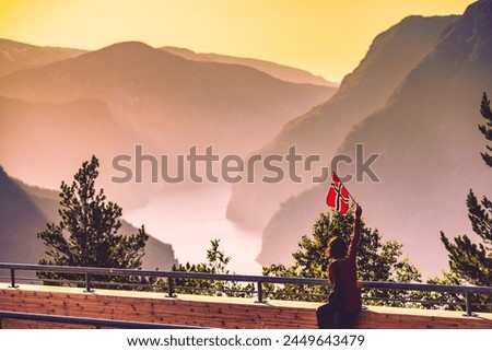 Tourist woman with norwegian flag enjoying fjord Aurlandsfjord view from Stegastein viewing point. National tourist route Aurlandsfjellet, Norway Royalty-Free Stock Photo #2449643479