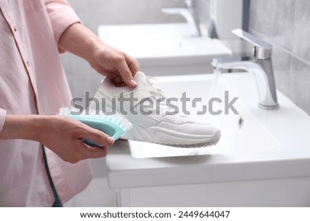 Woman washing stylish sneakers with brush in sink, closeup Royalty-Free Stock Photo #2449644047