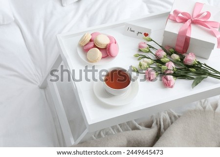 Tasty breakfast served in bed. Delicious macarons, tea, gift box, flowers and I Love You card on tray