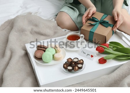 Tasty breakfast served in bed. Woman with gift box, desserts, tea, flowers and I Love You card at home, closeup
