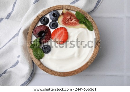 Bowl with yogurt, berries, fruits and mint on white tiled table, top view