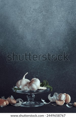 Artistic Garlic and Rosemary Display on Glass Stand. A glass stand presenting garlic bulbs and cloves with fresh rosemary, on a textured backdrop.