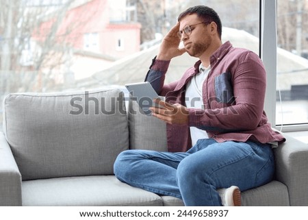 Portrait of tired male programmer working with tablet computer on sofa in office