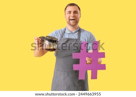 Male barista with hashtag and coffee pot on yellow background