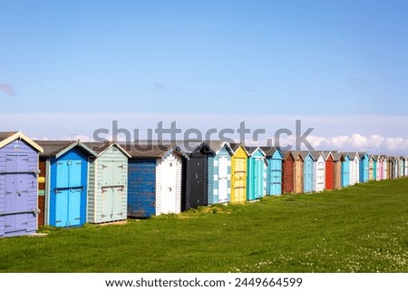 Beach huts along the Essex coast, Image shows a range of different colours and styles of beach huts on a warm spring day with slight cloud and blue sky Royalty-Free Stock Photo #2449664599