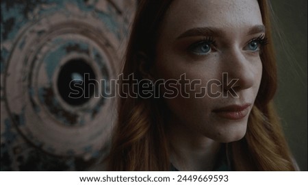 Portrait of a girl with red hair and blue eyes looking seriously into the distance, portrait with dark shades, no light. Photo in cold tones