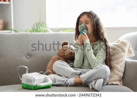 Little girl using nebulizer on sofa at home Royalty-Free Stock Photo #2449672341