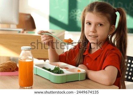 Cute little schoolgirl having lunch in classroom, closeup