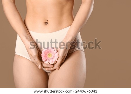 Young woman in panties with beautiful pink flower on brown background