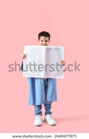 Cute little Asian boy in adult clothes with newspaper on pink background