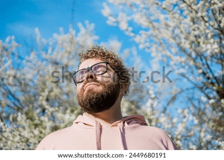 Handsome man outdoors portrait on background cherry blossoms or apple blossoms and blue spring sky. Millennial generation guy and new masculinity concept Royalty-Free Stock Photo #2449680191
