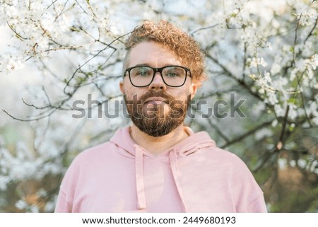 Handsome man outdoors portrait on background cherry blossoms or apple blossoms. Millennial generation guy and new masculinity concept Royalty-Free Stock Photo #2449680193