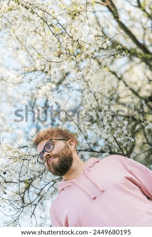 Handsome man outdoors portrait on background cherry blossoms or apple blossoms. Millennial generation guy and new masculinity concept Royalty-Free Stock Photo #2449680195