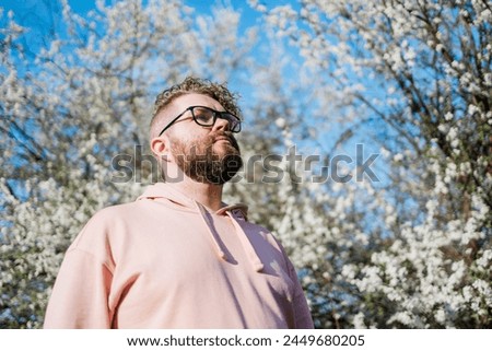 Handsome man outdoors portrait on background cherry blossoms or apple blossoms and blue spring sky. Millennial generation guy and new masculinity concept Royalty-Free Stock Photo #2449680205
