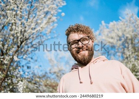 Handsome man outdoors portrait on background cherry blossoms or apple blossoms and blue spring sky. Millennial generation guy and new masculinity concept Royalty-Free Stock Photo #2449680219