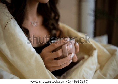 The picture captures a girl with a cup, her hands wrapped around it, savoring a moment of warmth and comfort. The soft lighting adds to the cozy ambiance.