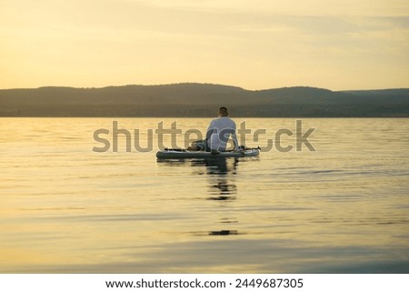  A man sits with his back facing on a paddleboard, relaxing and enjoying the sunset and vacation.