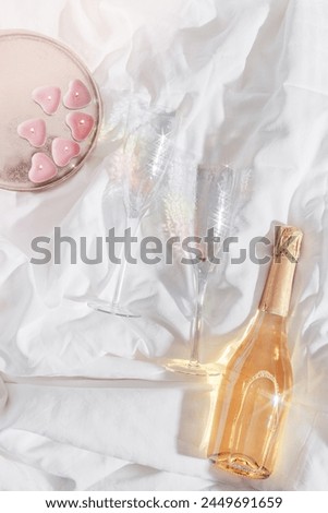 Rainbow color shining champagne glasses, white sparkling wine bottle, pink candles heart shape on white bedclothes. Lifestyle photo, star filter effect. Romance meeting, romantic holiday concept. 