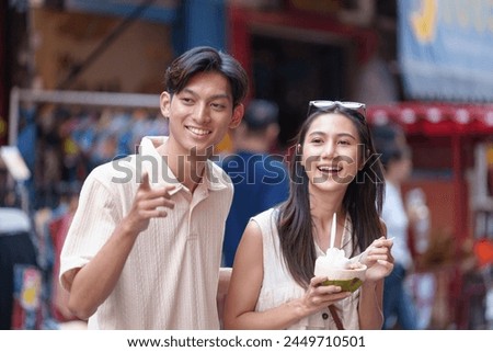 Tourist Asian couple walking around the market while eating Fruits from street stalls in the city market and crowds of people in the streets, alleys, tourist towns.