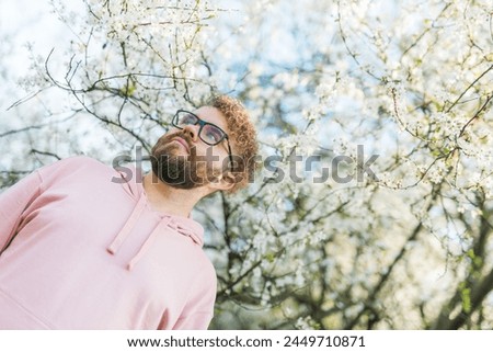 Handsome man outdoors portrait on background cherry blossoms or apple blossoms. Millennial generation guy and new masculinity concept. Copy space Royalty-Free Stock Photo #2449710871