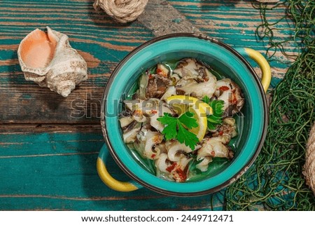 Rapana clam meat with oil, spices and greens. Healthy seafood rich of omega. Marine decor, hard light, dark shadow, old wooden boards, top view Royalty-Free Stock Photo #2449712471