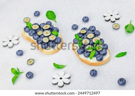 Fresh bread sandwiches with sweet blueberries, cream cheese and basil leaves. Good morning breakfast concept. White stone concrete background, flat lay, close up