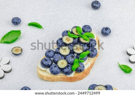 Fresh bread sandwiches with sweet blueberries, cream cheese and basil leaves. Good morning breakfast concept. White stone concrete background, flat lay, copy space