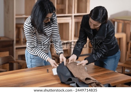 Two female designers selecting between leather and other materials for new furniture design. Royalty-Free Stock Photo #2449714835