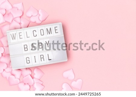 Welcome baby girl. Lightbox with letters and confetti in a heart shape on a pink pastel background. 