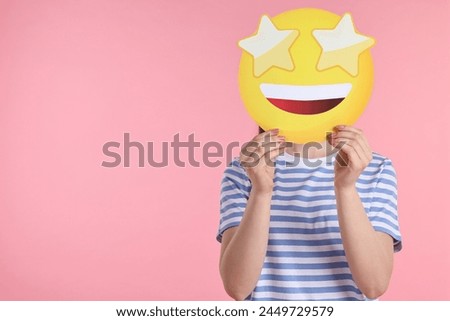 Woman holding emoticon with stars instead of eyes on pink background. Space for text