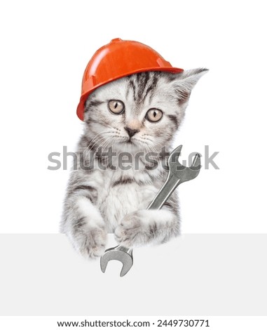 Cute kitten wearing hardhat holding the wrench and looking above blank white banner. Isolated on white background