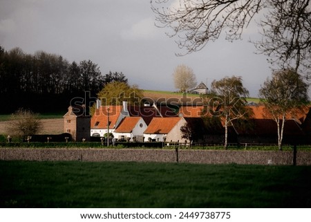 a picture of a farmhouse in belgium. with the background forest and fields, the sun has a warm feeling 