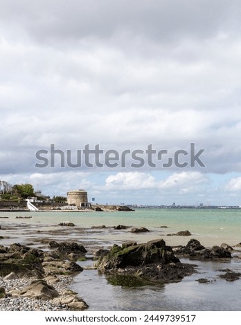 Large rocks and stones in the sea near Seapoint in Ireland. Tere are beach goers in the background around the Martello Tower with a cannon on top. Royalty-Free Stock Photo #2449739517