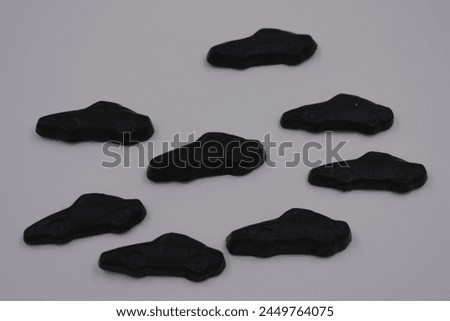 Unusual and non-standard jelly candies in the form of very black cars, cars located on a white plastic background. Royalty-Free Stock Photo #2449764075