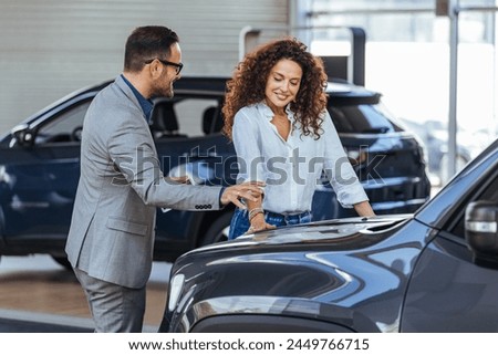 Woman in the showroom enjoying luxury car. Happy salesman selling the car to his female customer in a showroom. Auto business, car sale, consumerism and people concept
