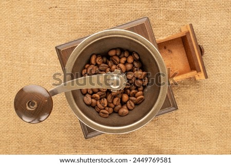 One manual, wooden coffee grinder with coffee beans on a jute cloth, macro, top view. Royalty-Free Stock Photo #2449769581