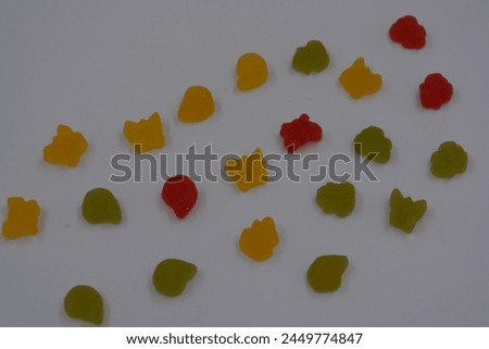 Unusual and non-standard, small jelly candies in the form of yellow, red, green butterflies, shells, flowers located on a white plastic background. Royalty-Free Stock Photo #2449774847