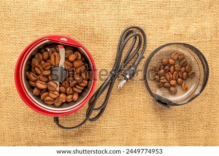 One electric coffee grinder with coffee beans on a jute cloth, macro, top view. Royalty-Free Stock Photo #2449774953