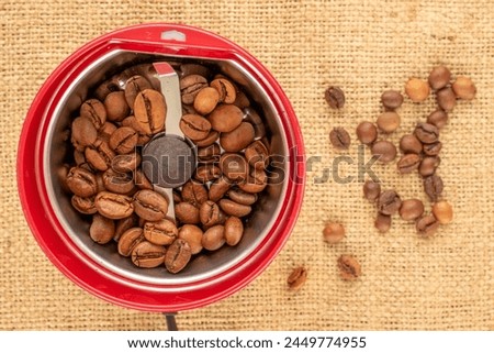 One electric coffee grinder with coffee beans on a jute cloth, macro, top view. Royalty-Free Stock Photo #2449774955