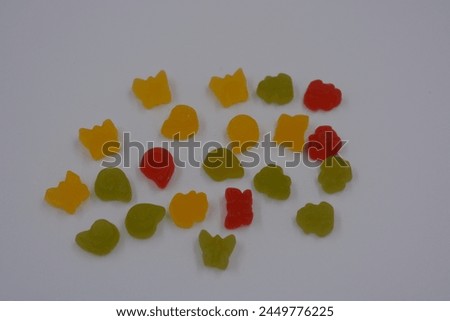 Unusual and non-standard, small jelly candies in the form of yellow, red, green butterflies, shells, flowers located on a white plastic background. Royalty-Free Stock Photo #2449776225