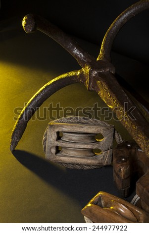 Anchor and marine pulley in studio light : grazing yellow light and black background