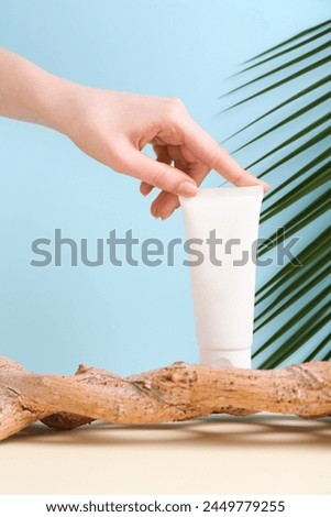 Woman with tube of cream and plant against light blue background, closeup